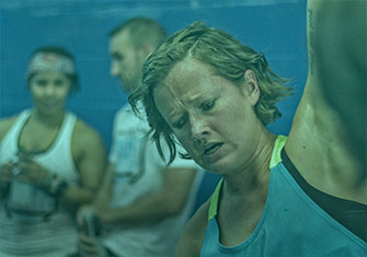 Sara doing dumbbell snatches with focused look as people watch